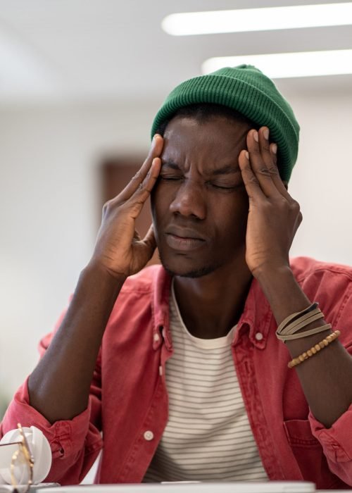 Exhausted black student man suffering from anxiety or panic attack after long prepare exam on laptop Stressed tired African American student man touching temples have headache after long time preparing for test in college library. Frustrated black hipster male feels nervous afraid of exam failure.